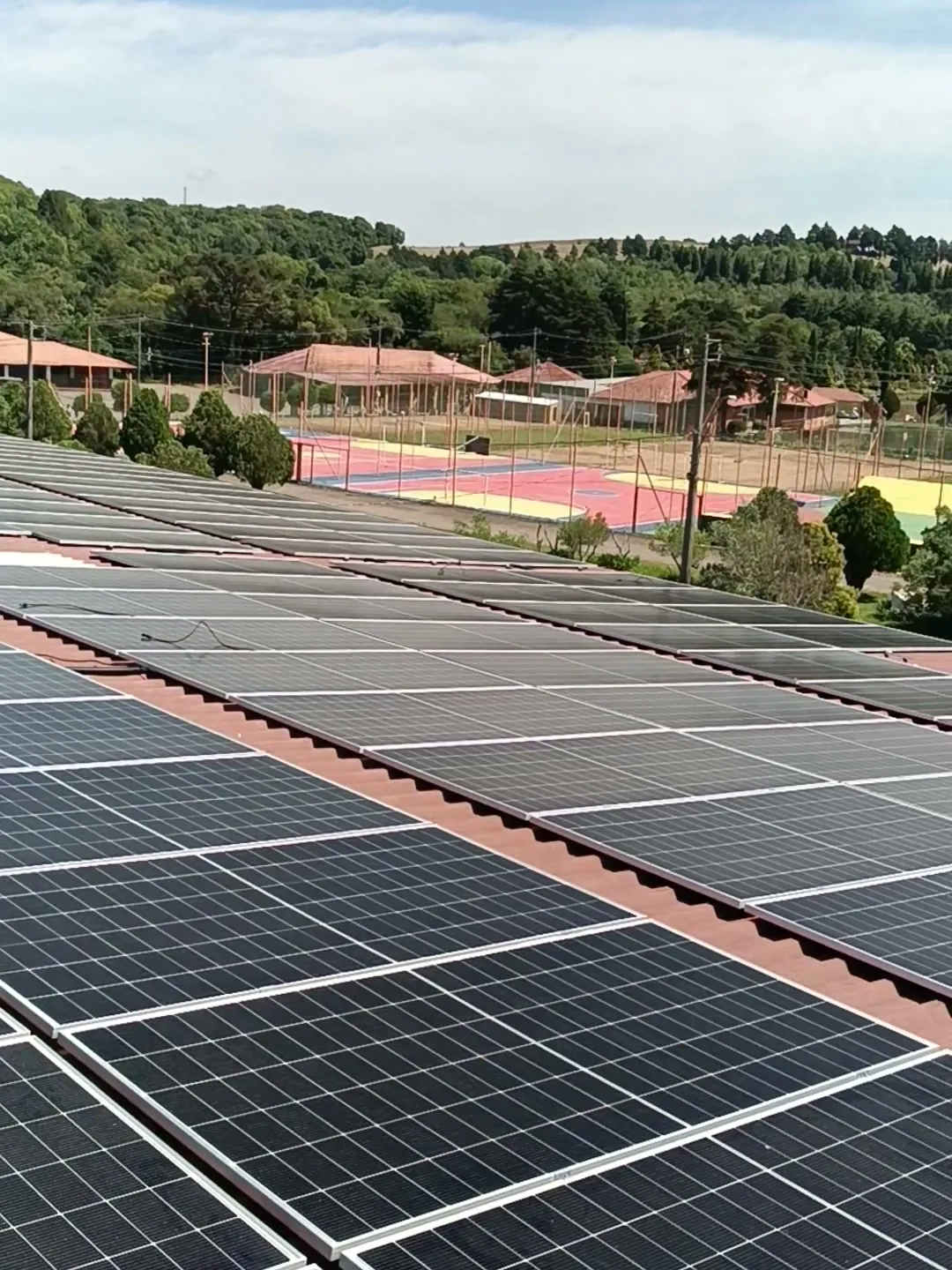 Telhado coberto de painéis solares instalados pela Energy Volt, com quadras e morros ao fundo