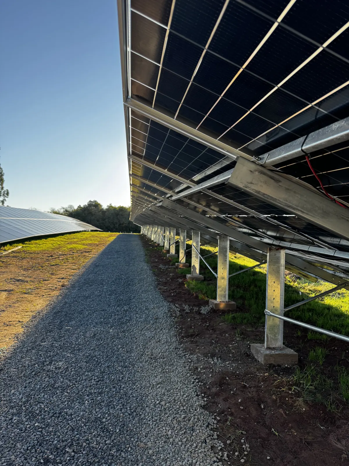 Corredor de brita sob uma longa fileira de painéis solares de uma usina instalada pela Energy Volt